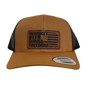 May include: A brown and black trucker hat with a brown leather patch that says "Whiskey Beer Guns & Freedom" with an American flag design.