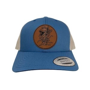 May include: A blue and white trucker hat with a brown leather patch featuring a black and white illustration of a plant monster with a toothy mouth. The patch has the text "The Authentic Snapback" on it.