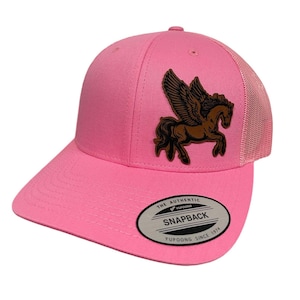 May include: Pink trucker hat with a brown leather winged horse patch and a black and white "The Authentic Yupoong Snapback Since 1974" label.