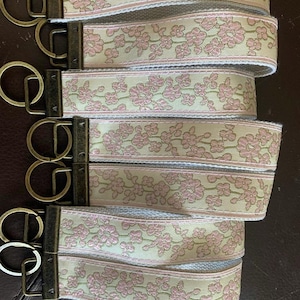 May include: Five keychains with antique gold key rings and a light beige fabric strap with a pink floral pattern.