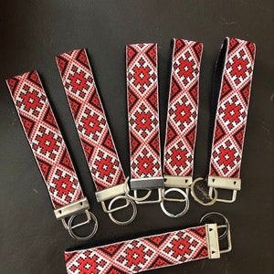 May include: Six keychains with a red, white, and black geometric design. Each keychain has a silver-coloured metal ring and clasp. The keychains are displayed on a dark surface.