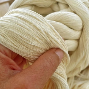 May include: A thick, off-white fiber bundle featuring a braided, rope-like construction. The material has a smooth, slightly lustrous texture with visible individual strands running parallel along the length of the twisted, chunky cord.