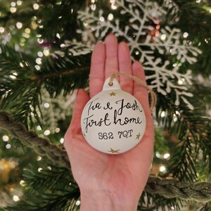 May include: White Christmas bauble with gold stars and the text "Tia & Josh First Home S62 7QT"