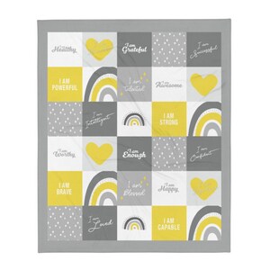 May include: A gray and yellow throw blanket with a patchwork design featuring positive affirmations like "I am strong", "I am worthy", and "I am loved".