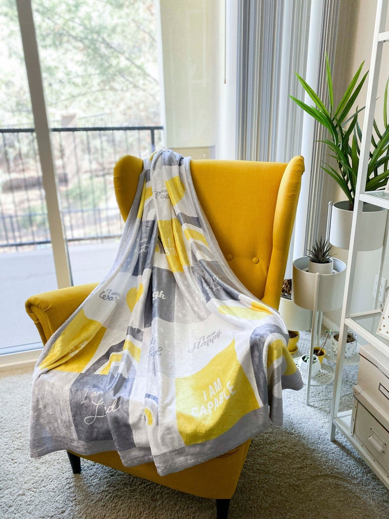 May include: A yellow armchair with a gray and yellow throw blanket. The blanket has the words "I am capable", "I am happy", "I am loved", and "I am enough" printed on it.