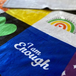 May include: A colorful patchwork quilt with different squares featuring a green heart, a rainbow, and the words "I am Enough" in white on a blue square.