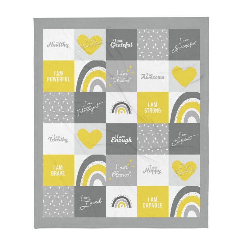 May include: A gray and yellow throw blanket with a patchwork design featuring positive affirmations like "I am strong", "I am worthy", and "I am loved".