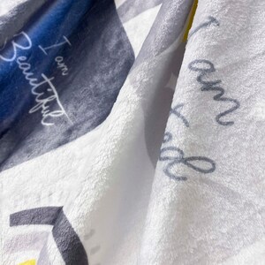 May include: A white, gray, and yellow fleece blanket with the text "I am Beautiful" printed on it.