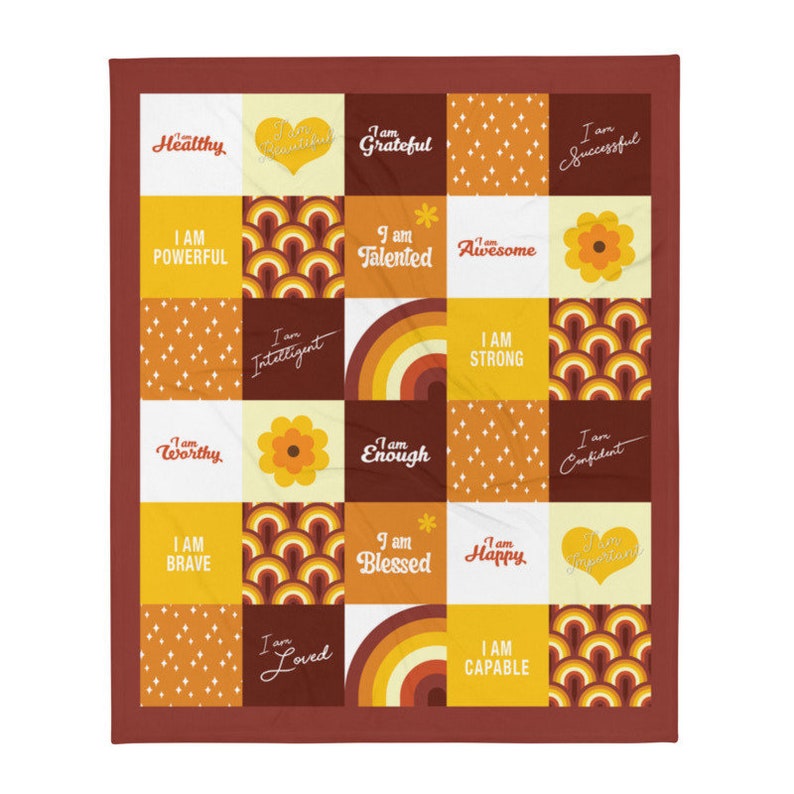 May include: A colorful throw blanket with a patchwork design featuring positive affirmations like "I am strong", "I am worthy", and "I am loved". The blanket is made up of squares with different patterns and colors, including yellow, orange, brown, and white.