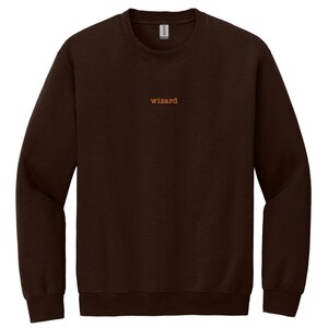 May include: A dark brown sweatshirt with the word "wizard" in orange lettering across the chest. The long-sleeved crew neck top is made of a soft material.
