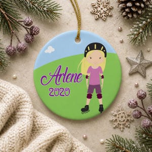 May include: A round ceramic ornament featuring a cartoon girl in roller skates, wearing a helmet and protective gear. The ornament has a green and blue background with the name "Arlene" and the year "2020" in purple script.