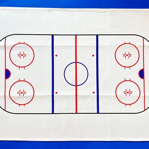 May include: White cotton tea towel with a black and red hockey rink design. The rink has two blue lines, a red center line, and two face-off circles.