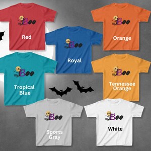 May include: Six different color t-shirts with a Halloween-themed design featuring a ghost, a tree, and the word "Boo". The colors are red, orange, royal blue, tropical blue, Tennessee orange, and sports gray.