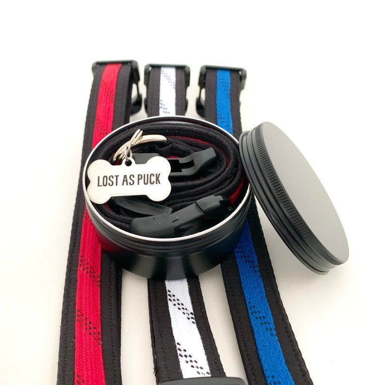 May include: Three dog collars in red, white, and blue with a black metal container with a dog tag that says "Lost as Puck".