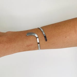 May include: A silver bracelet with a curved design that resembles a hockey stick.
