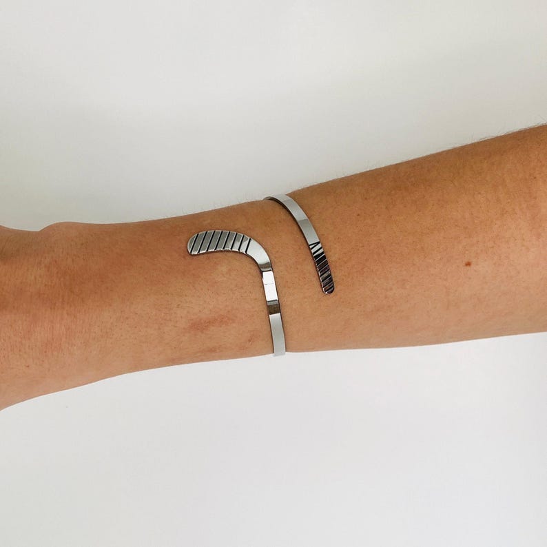 May include: A silver bracelet with a curved design that resembles a hockey stick.