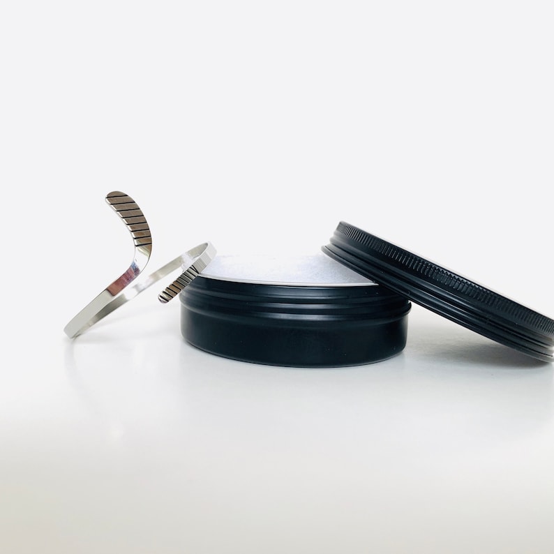 May include: A silver bracelet with a geometric design, in a black tin container with a lid.