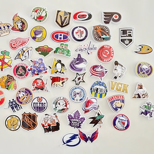 May include: A collection of colorful hockey team logo stickers. The stickers feature logos from teams like the Capitals, Blues, Oilers, Maple Leafs, and Rangers. The stickers are perfect for decorating laptops, water bottles, or anything else you can think of.