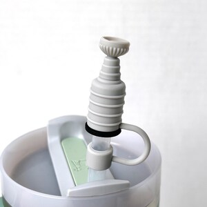May include: A white plastic water bottle with a gray silicone spout and a black ring around the spout. The bottle has a green lid and a white handle.
