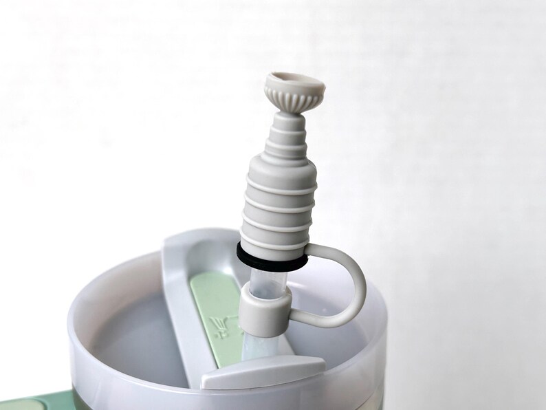 May include: A white plastic water bottle with a gray silicone spout and a black ring around the spout. The bottle has a green lid and a white handle.