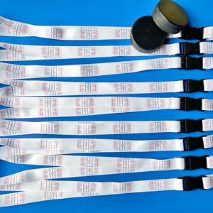 May include: Ten white lanyards with a hockey rink design printed on them. Each lanyard has a black breakaway clip and a silver swivel hook. Two black hockey pucks are also included in the image.