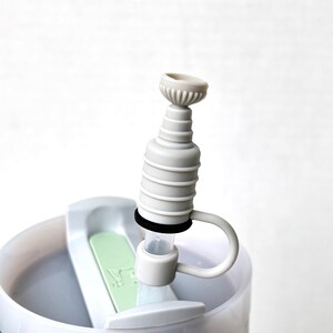 May include: Close-up of a white plastic bottle with a gray and white silicone spout. The spout has a ring around it and a small handle.