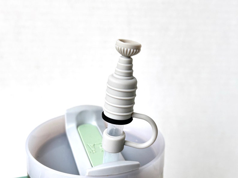 May include: Close-up of a white plastic bottle with a gray and white silicone spout. The spout has a ring around it and a small handle.