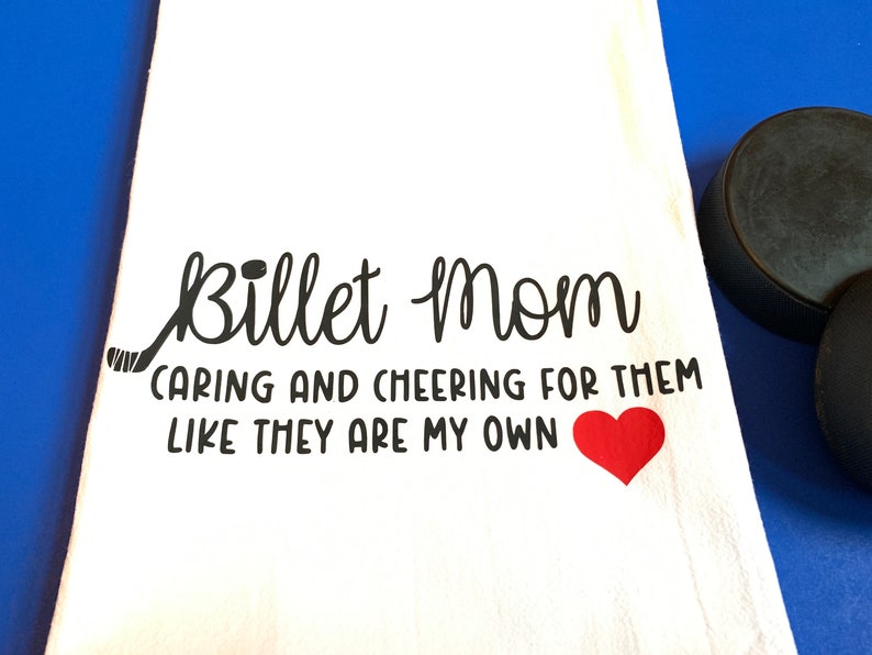 May include: White kitchen towel with black text that reads "Billet Mom Caring and Cheering for Them Like They Are My Own" with a black hockey stick and a red heart.