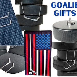 May include: A collection of goalie gifts featuring hockey stick and puck designs. The gifts include a tie bar, a necklace, a hat, a flag, and a puck. The flag is an American flag with a hockey stick design. The text "GOALIE GIFTS" is displayed in blue letters.