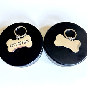 May include: Two black dog tag holders with silver bone-shaped tags. One tag says "Lost as Puck".