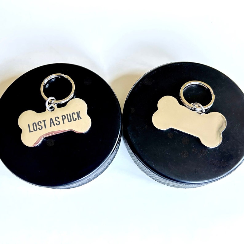 May include: Two black dog tag holders with silver bone-shaped tags. One tag says "Lost as Puck".