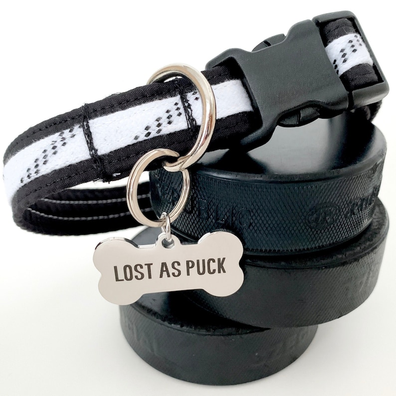 May include: Black and white hockey-themed dog collar with a silver bone-shaped tag that reads "LOST AS PUCK".