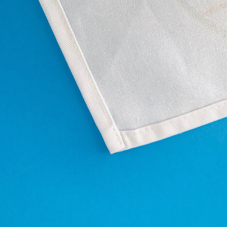 May include: Close-up of a white fabric with a stitched edge. The fabric is against a bright blue background.