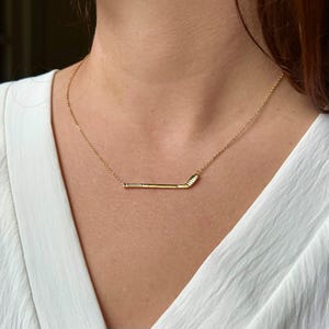 May include: A gold necklace with a hockey stick pendant.