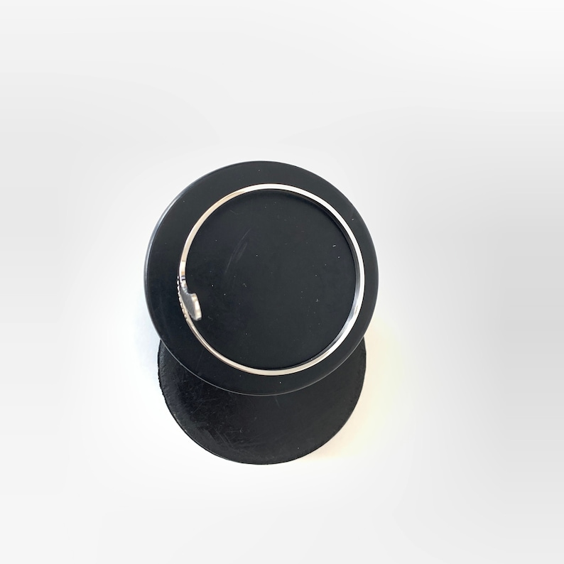 May include: A silver bangle bracelet on a black display stand.