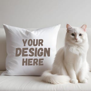 Op de afbeelding: Een wit kussen met de tekst "YOUR DESIGN HERE" op een witte bank met een witte kat die op de bank zit.