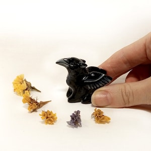 May include: Black obsidian griffin figurine with detailed wings. The figurine is about 2 inches tall and is sitting on a white surface.