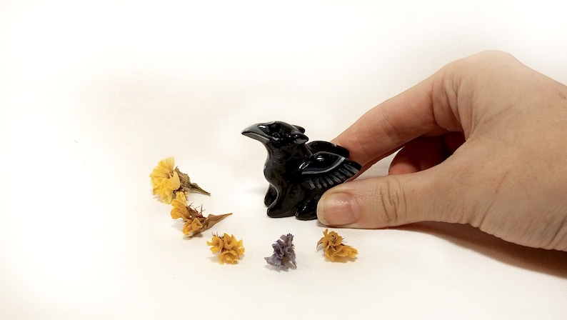 May include: Black obsidian griffin figurine with detailed wings. The figurine is about 2 inches tall and is sitting on a white surface.