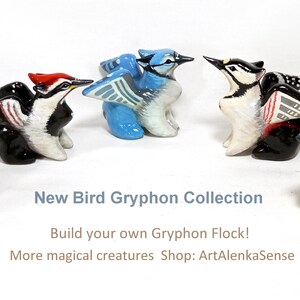 May include: A collection of ceramic bird gryphon figurines in various colors, including blue, yellow, black, and red. The figurines are arranged in a semi-circle. Text on the image reads "New Bird Gryphon Collection" and "Build your own Gryphon Flock!"