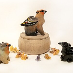 May include: Three ceramic bird figurines with wings. The birds are painted in shades of brown, black, and yellow. The birds are sitting on a wooden base.