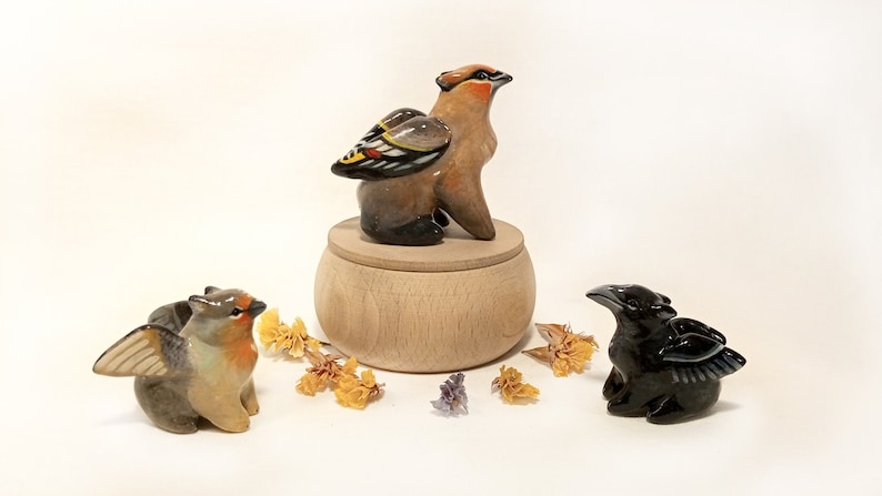 May include: Three ceramic bird figurines with wings. The birds are painted in shades of brown, black, and yellow. The birds are sitting on a wooden base.