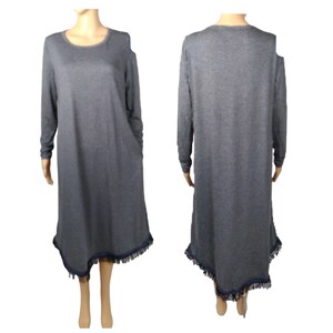 May include: A gray long-sleeve dress with a round neckline and asymmetrical hemline. The hemline is trimmed with a dark blue fringe. The dress has a relaxed fit and is made of a soft material.