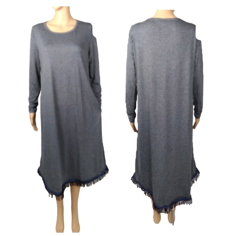 May include: A gray long-sleeve dress with a round neckline and asymmetrical hemline. The hemline is trimmed with a dark blue fringe. The dress has a relaxed fit and is made of a soft material.