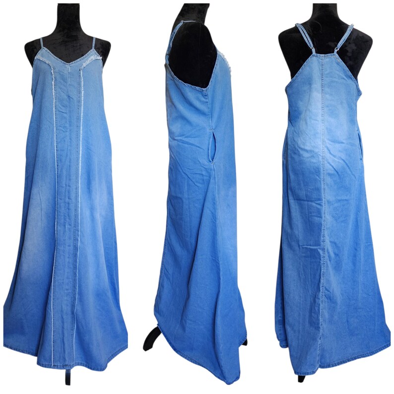 May include: A light blue denim maxi dress with thin straps and a V-neckline. The dress features white stitching details and a flowing skirt. The dress is displayed on a black mannequin, showcasing its design from multiple angles.