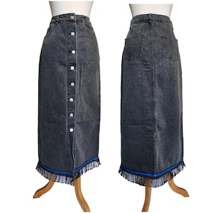 May include: A dark gray denim skirt with a button-up front and a fringed hemline. The skirt has a high waist and a straight silhouette. The hemline features a blue ribbon detail and black fringe.