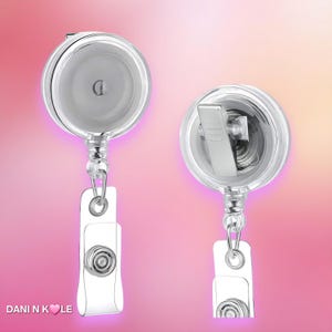 May include: Two clear plastic badge reels with retractable cords and metal belt clips. The front view shows a circular housing, while the back view displays the metal clip mechanism. The text DANI N KOLE with a heart icon is visible at the bottom.