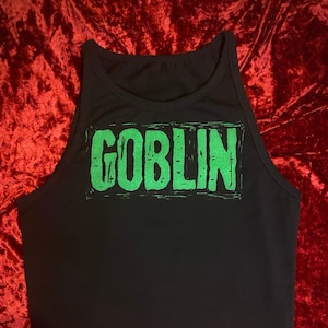 Puede incluir: Camiseta de tirantes negra con un gráfico verde que dice "GOBLIN" en una fuente desgastada.