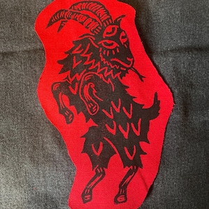 May include: A red fabric patch with a black silhouette of a goat with horns. The goat is standing on its hind legs and has a fierce expression.