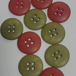 May include: A collection of ten round, four-hole buttons in alternating shades of muted olive green and reddish-pink. Each button features a smooth, matte surface with a slightly recessed center area containing four evenly spaced holes for attachment.