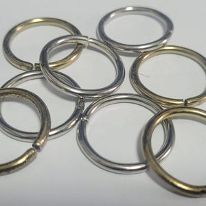 Pu&ograve; includere: Una collezione di anelli aperti in varie finiture metalliche, tra cui argento e oro. Gli anelli sono sparsi su una superficie bianca, mostrando la loro forma circolare e il design aperto, ideali per la creazione di gioielli o lavori artigianali.